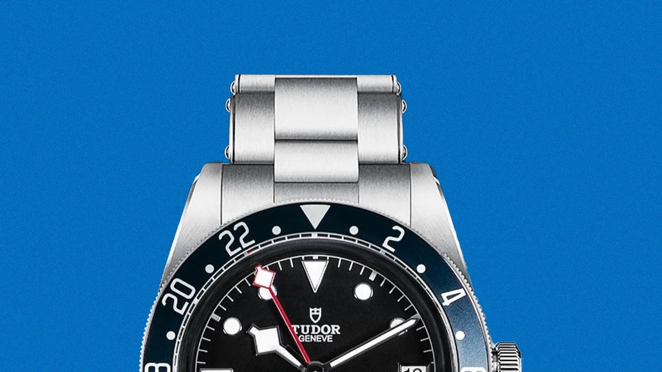 Stainless steel Tudor wristwatch with black dial, red-tipped GMT hand, and blue bezel with white numerals.