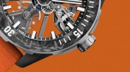 Close-up of a mechanical watch with a carbon fiber bezel, visible gears, and an orange textured strap.