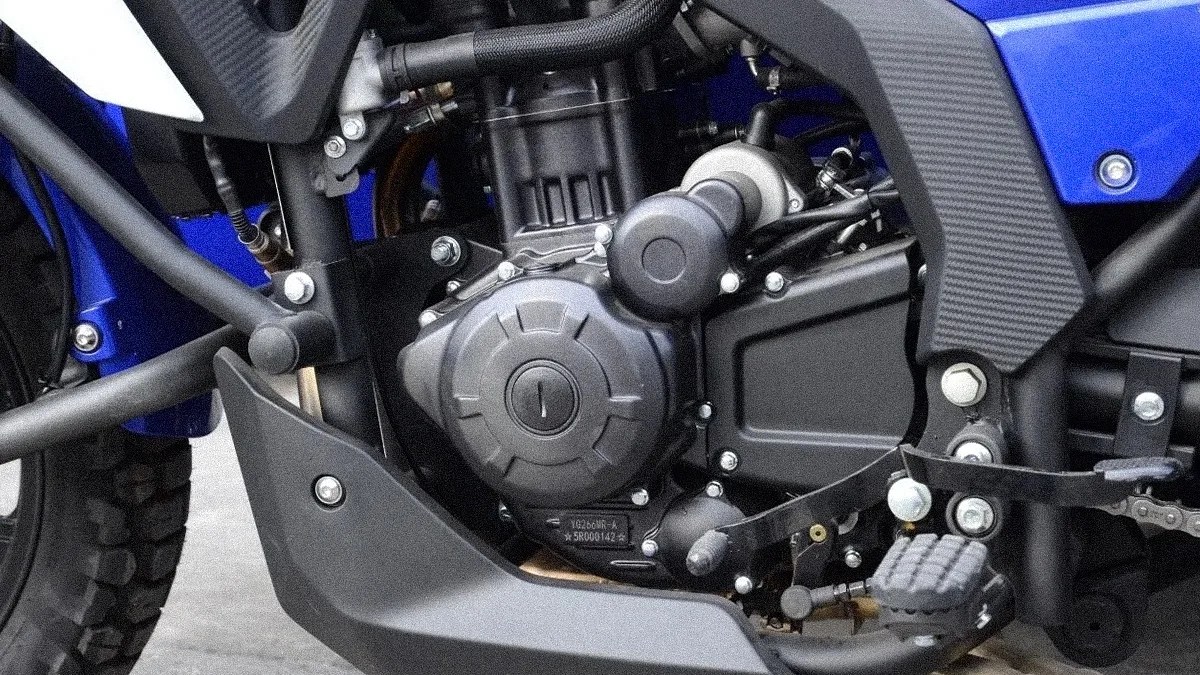 Close-up of a black motorcycle engine with visible bolts and a foot peg on a blue bike frame.