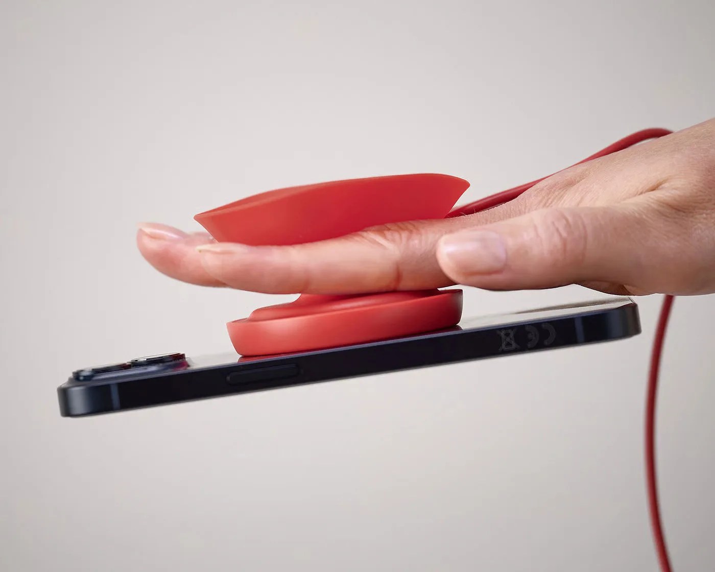 Hand holding a black smartphone with a red suction cup phone grip attached.