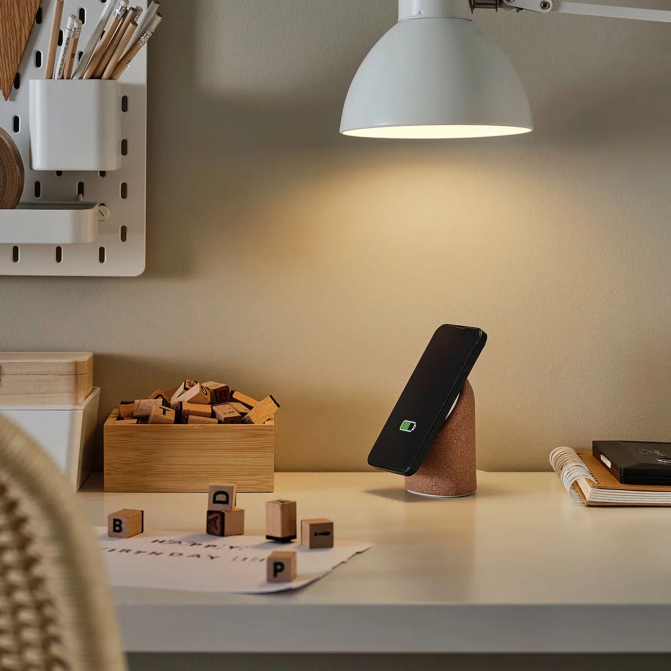 Black smartphone charging on a cork wireless charger on a beige desk under a white lamp.