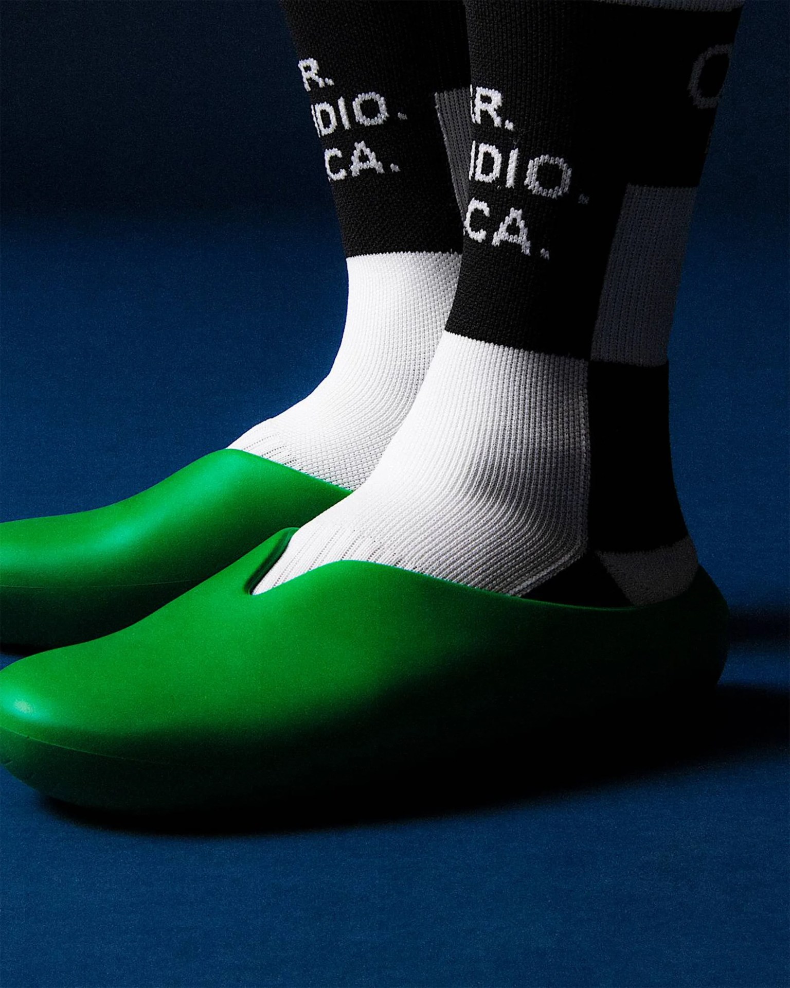 Bright green slip-on shoes worn with black and white socks featuring white text on a dark blue floor.