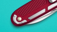 Close-up of a red Swiss Army knife handle with textured grip and partially visible blade on a turquoise background.