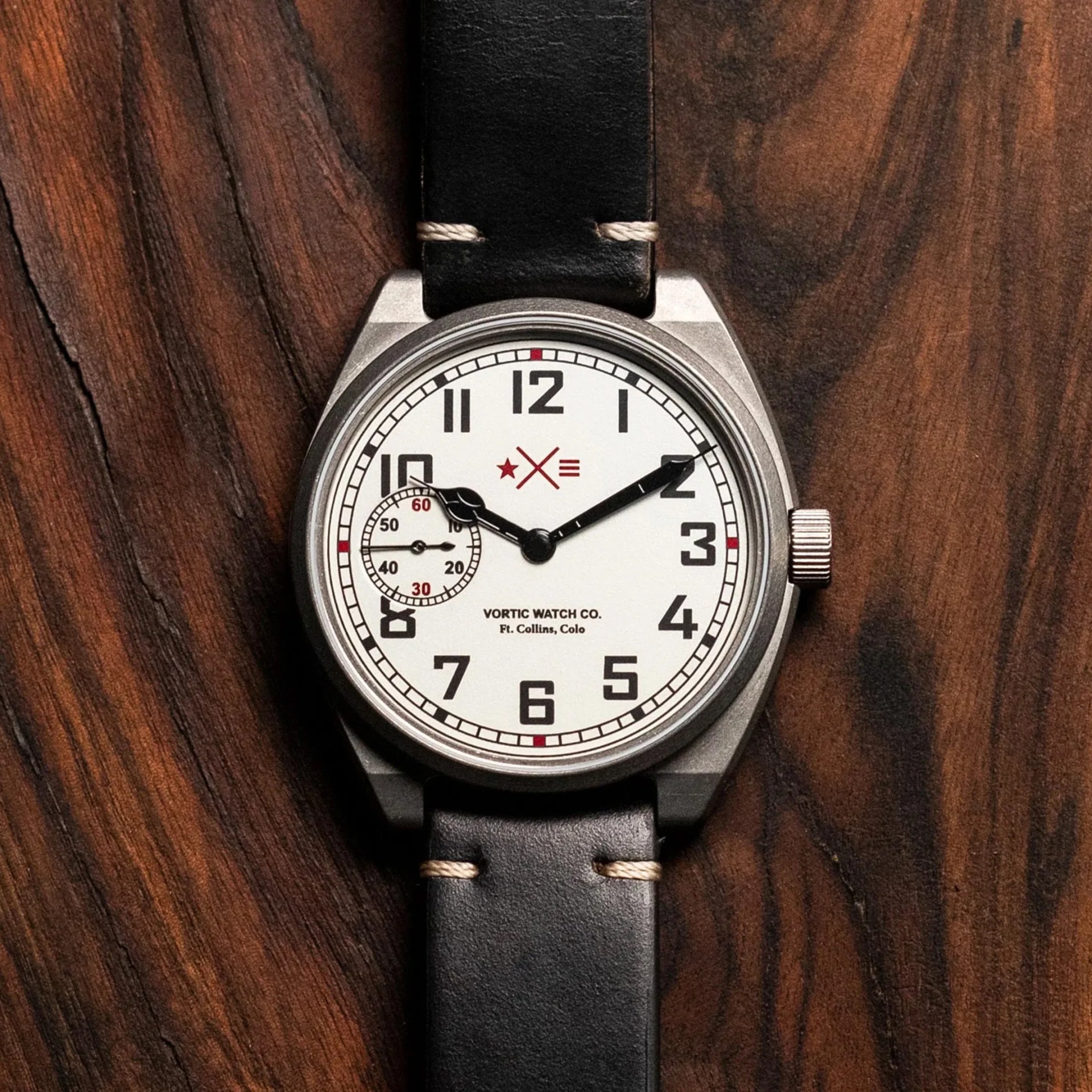 Round silver wristwatch with white dial, black numerals, black leather strap, and small seconds subdial at 9 o'clock.