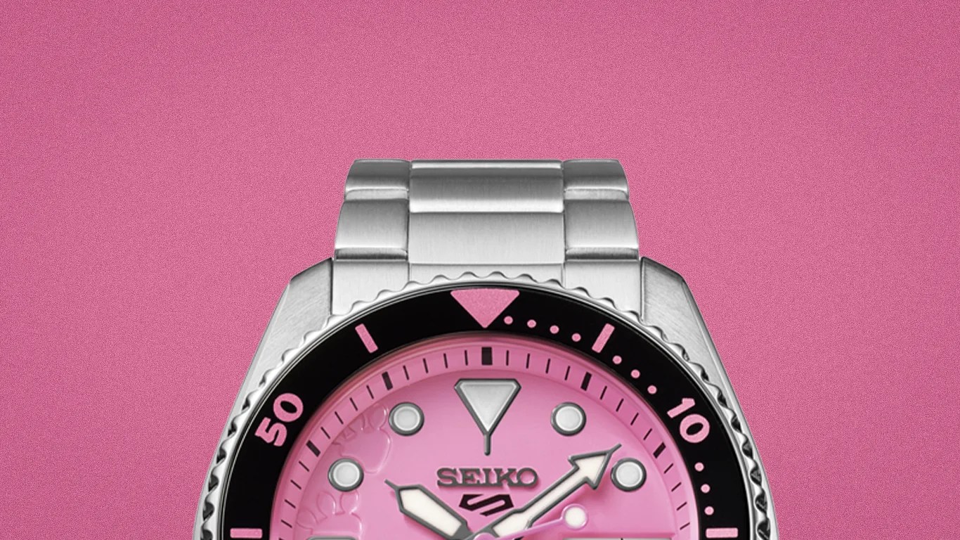 Silver Seiko wristwatch with a pink dial and black bezel on a pink background.