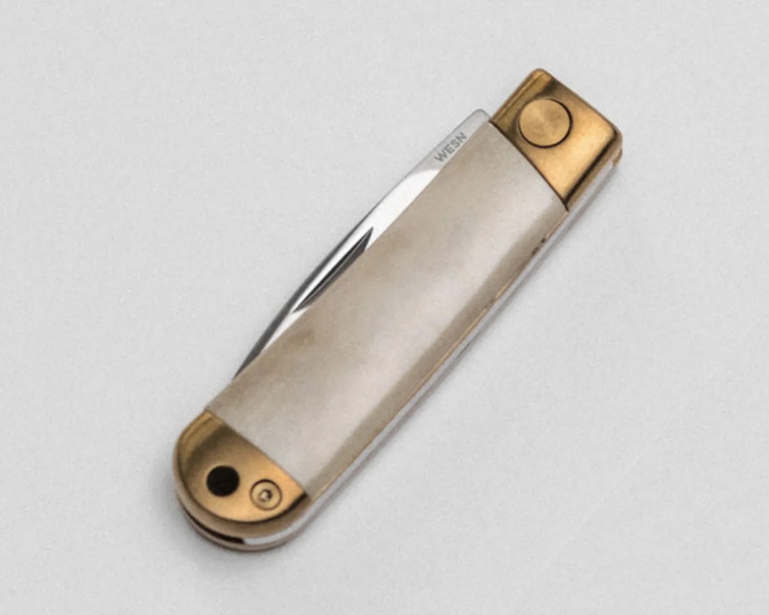 Compact folding pocket knife with a silver handle and brass accents on a light gray surface.