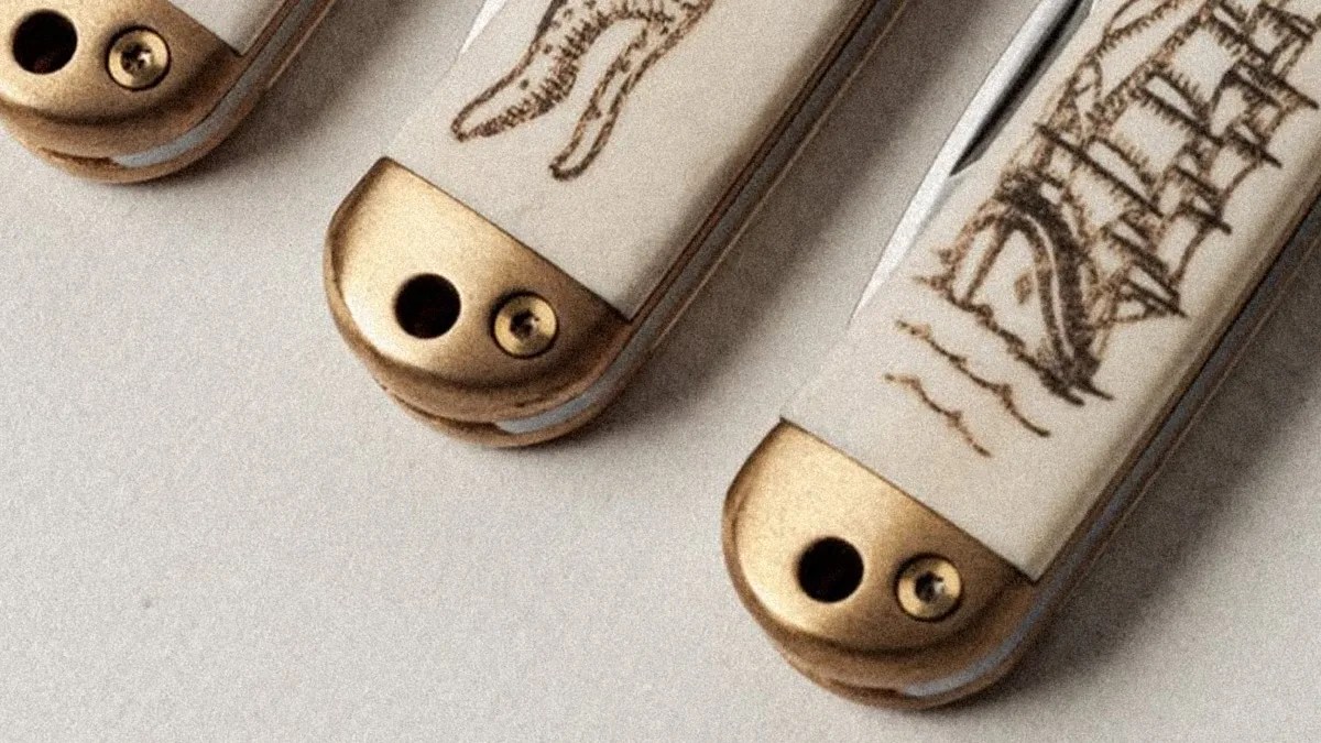 Close-up of three ivory-handled pocket knives with brass bolsters, each handle engraved with different designs.
