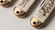 Close-up of three ivory-handled pocket knives with brass bolsters, each handle engraved with different designs.