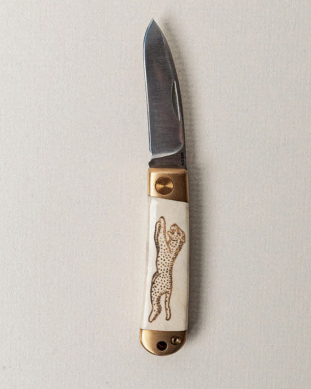 Folding pocket knife with a metal blade and a white handle featuring an engraved leaping cheetah design.