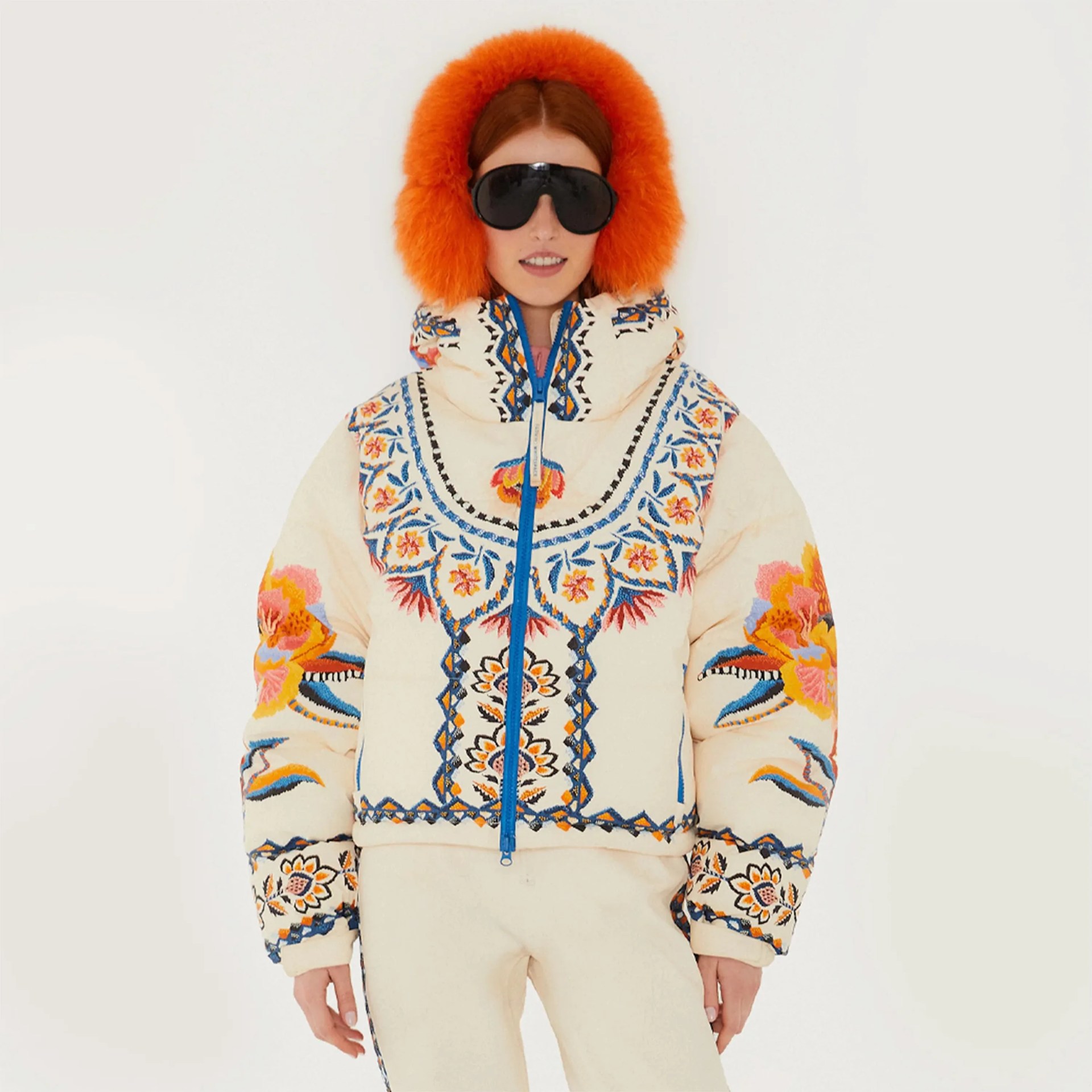 Cream puffer jacket with colorful floral embroidery and blue zipper worn with orange earmuffs and black sunglasses.