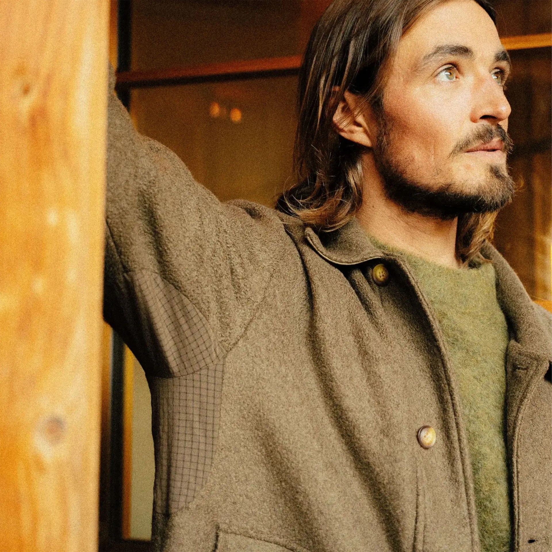 Man wearing a brown textured jacket with button closure and green fuzzy sweater underneath.