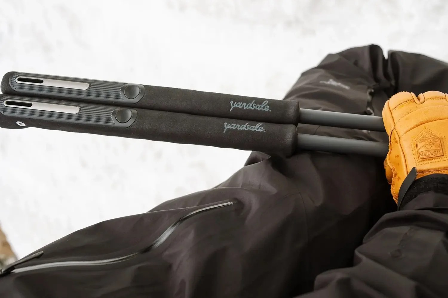 Pair of black snow shovel handles with "yardsale" branding held by a person wearing a black jacket and tan gloves.