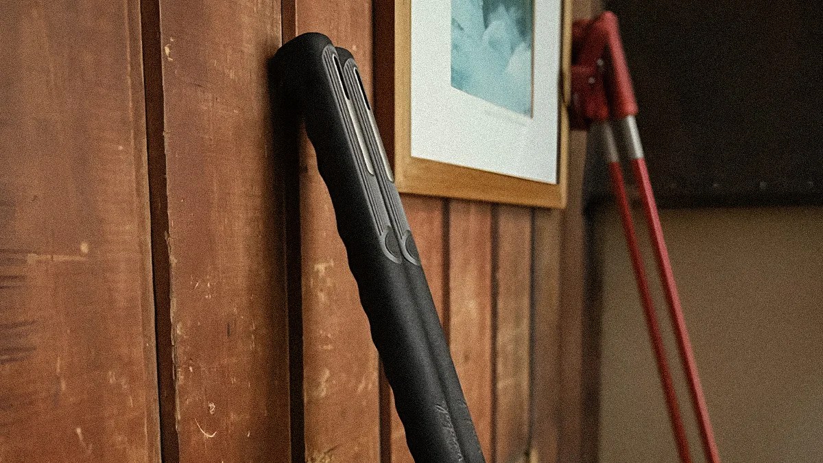 Black rubber-handled kitchen tongs hanging on a wooden wall near a framed picture and red-handled garden shears.