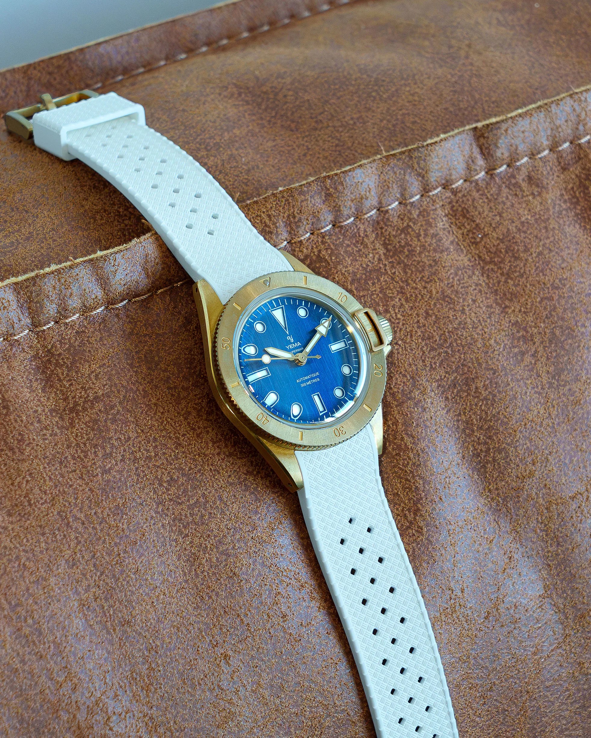 Bronze Yema wristwatch with blue dial and white textured rubber strap on brown leather surface.
