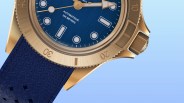 Close-up of a gold-tone watch with a blue dial, luminous markers, and a textured blue rubber strap.