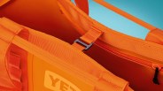 Close-up of an orange YETI bag showing handles, zipper, and interior strap with buckle.