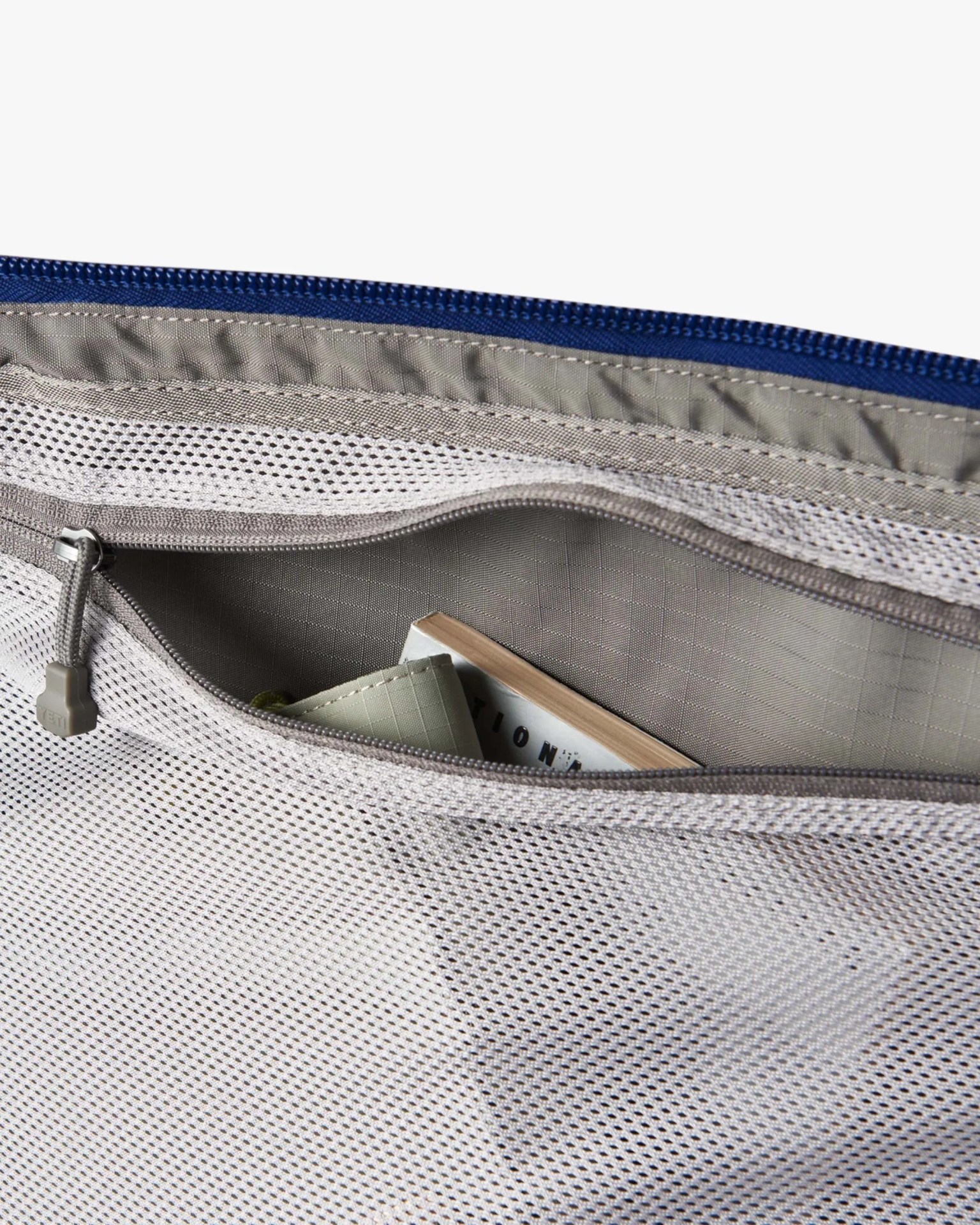Close-up of a gray mesh zippered pocket containing a partially visible book and a green item inside a bag.