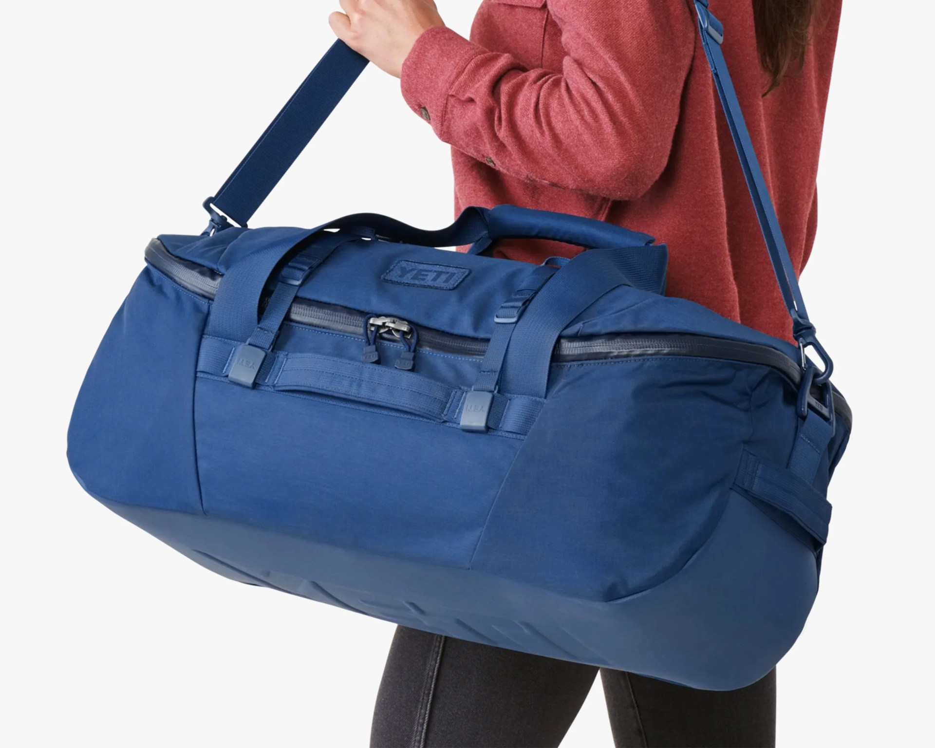 Blue YETI duffel bag with padded shoulder strap worn by a person in a red jacket.