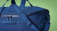 Navy blue YETI duffel bag with padded adjustable shoulder strap and zipper closure against a green background.