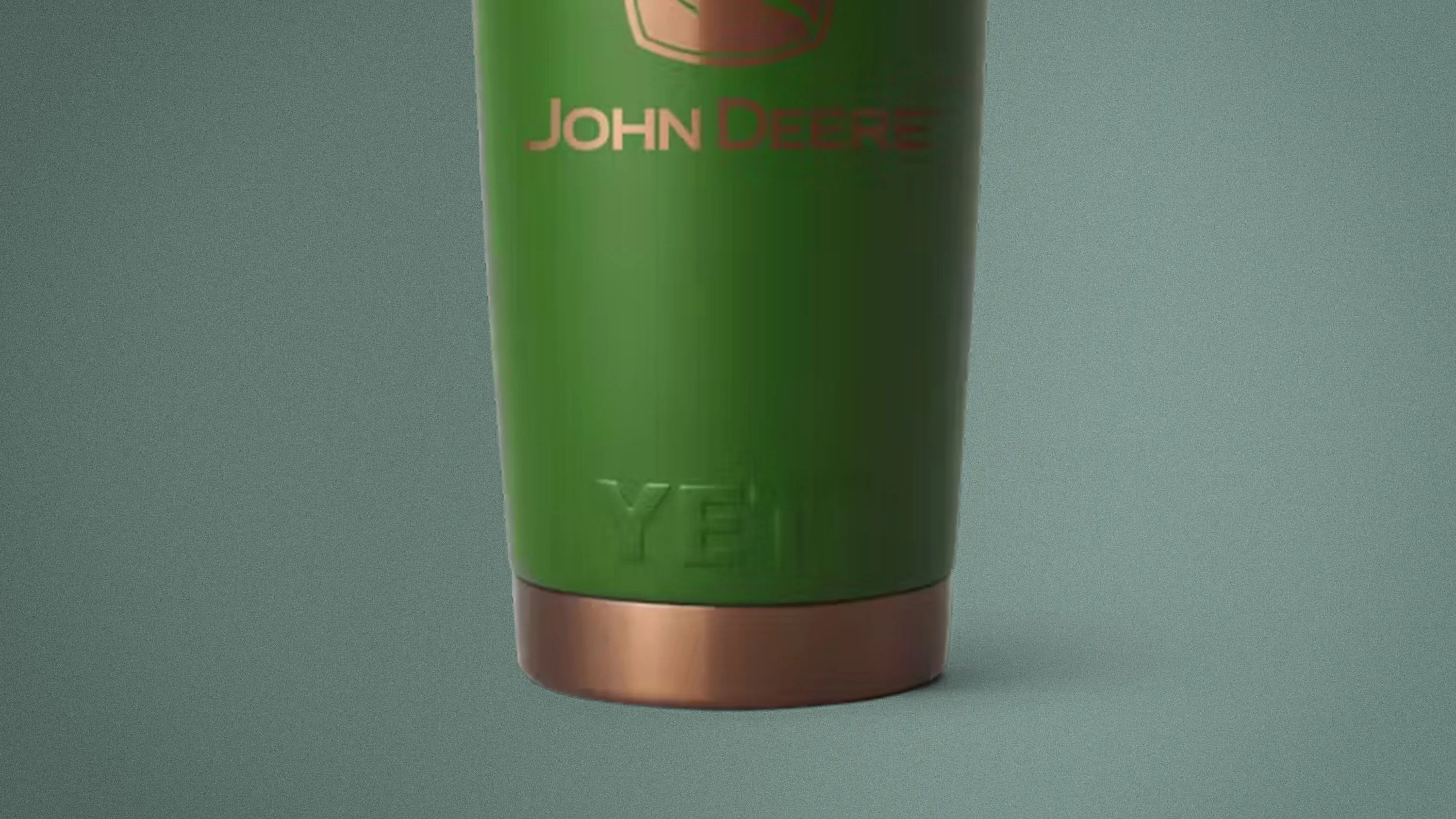 Green John Deere Yeti tumbler with copper-colored base on a gray surface.