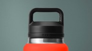 Close-up of a black plastic handle lid on a stainless steel and bright orange YETI bottle.