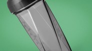 Gray translucent plastic blender jar with measurement markings and a gray lid on a green background.