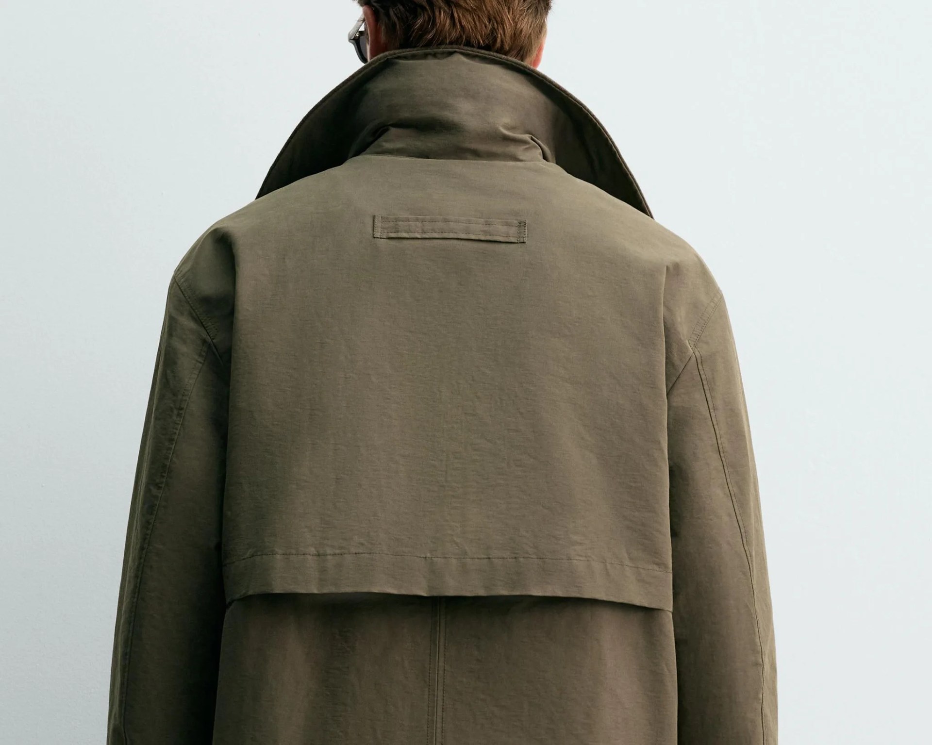Olive-green jacket with high collar and back yoke detail worn by a person facing away.
