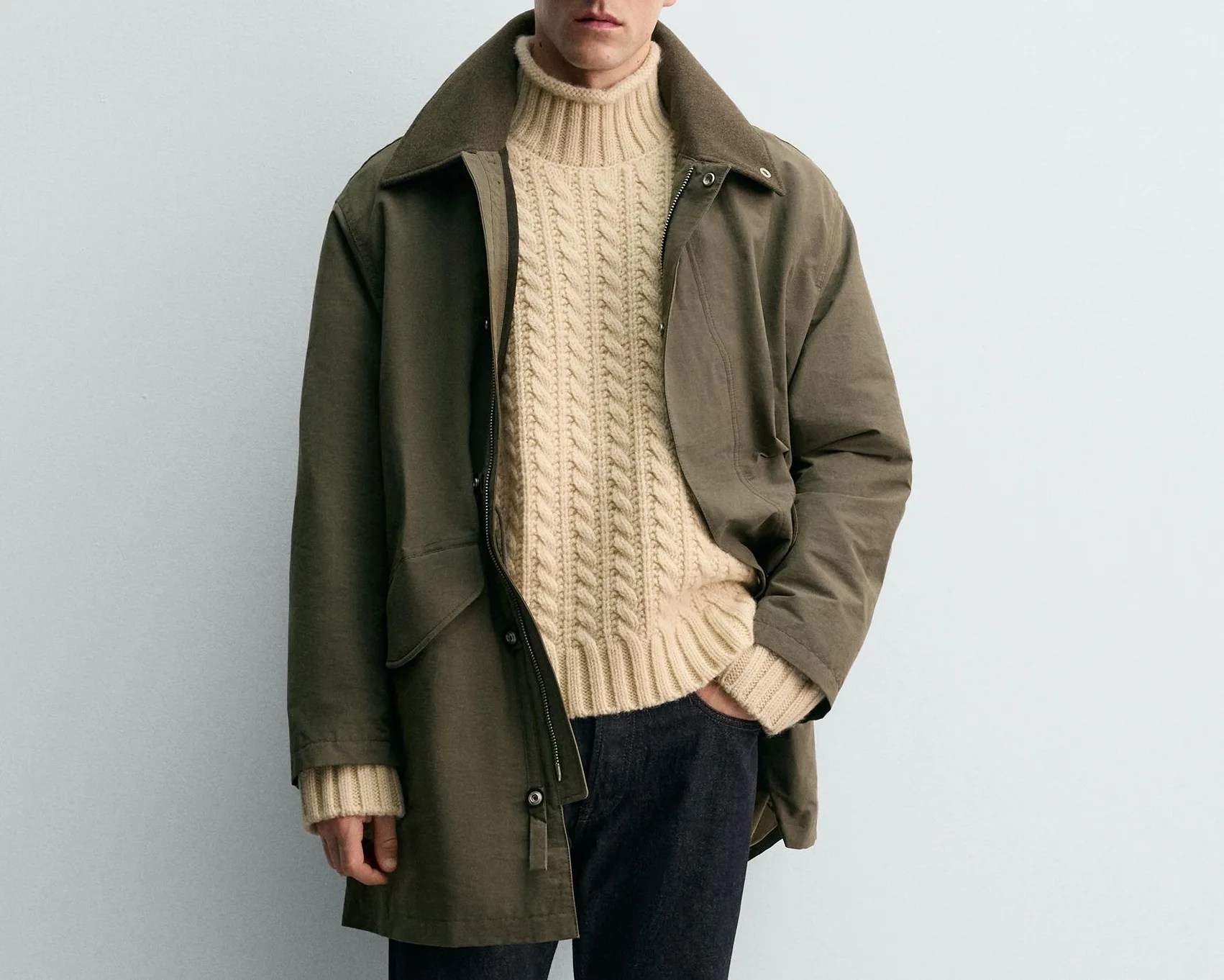 Olive green oversized jacket over a cream cable-knit turtleneck sweater and dark pants.