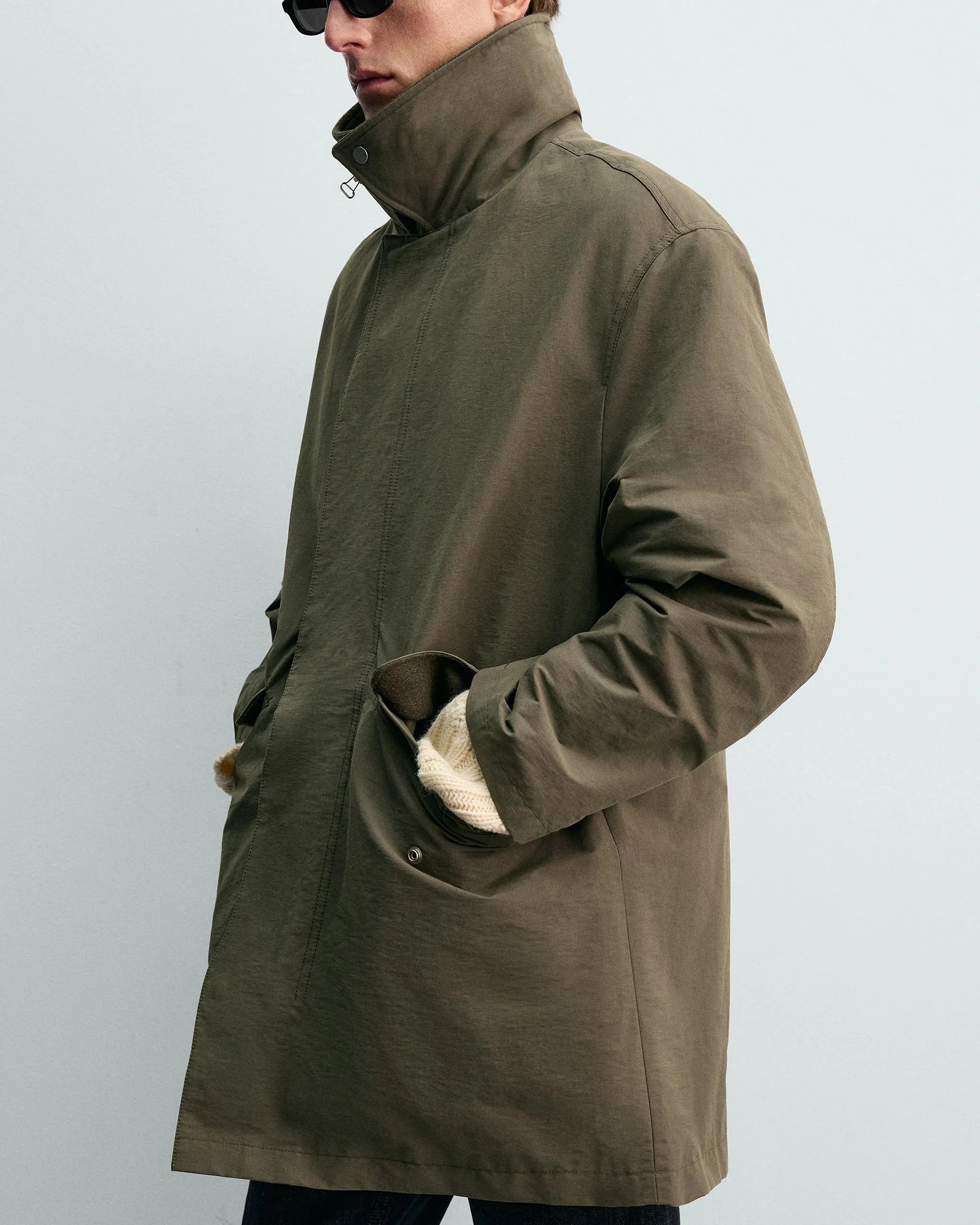 Olive-green high-collar coat with snap buttons and hands in pockets, worn by a person.