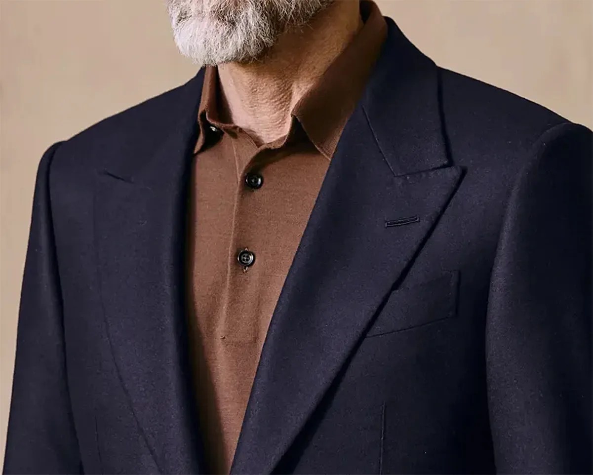 Close-up of a man wearing a dark navy blazer over a brown buttoned shirt.