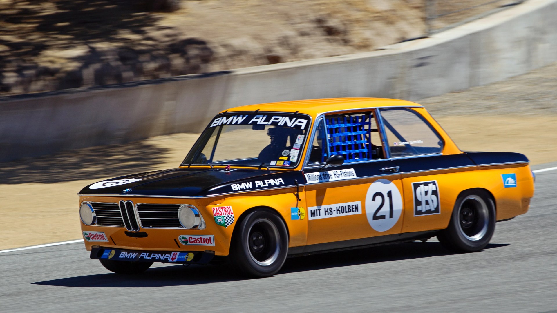Orange and black BMW Alpina race car number 21 on a racetrack with sponsor decals.
