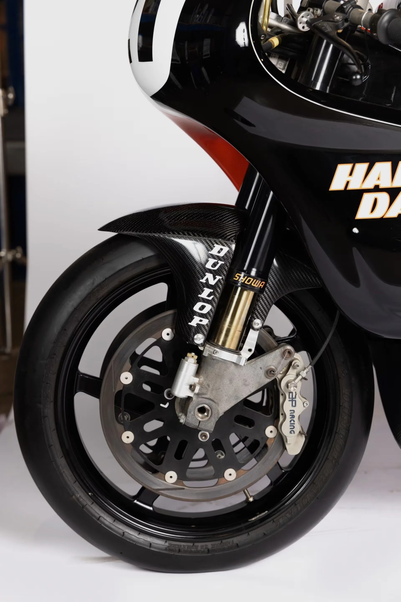 Close-up of a black motorcycle front wheel with Dunlop carbon fiber fender, Showa suspension, and GP Racing brake caliper.