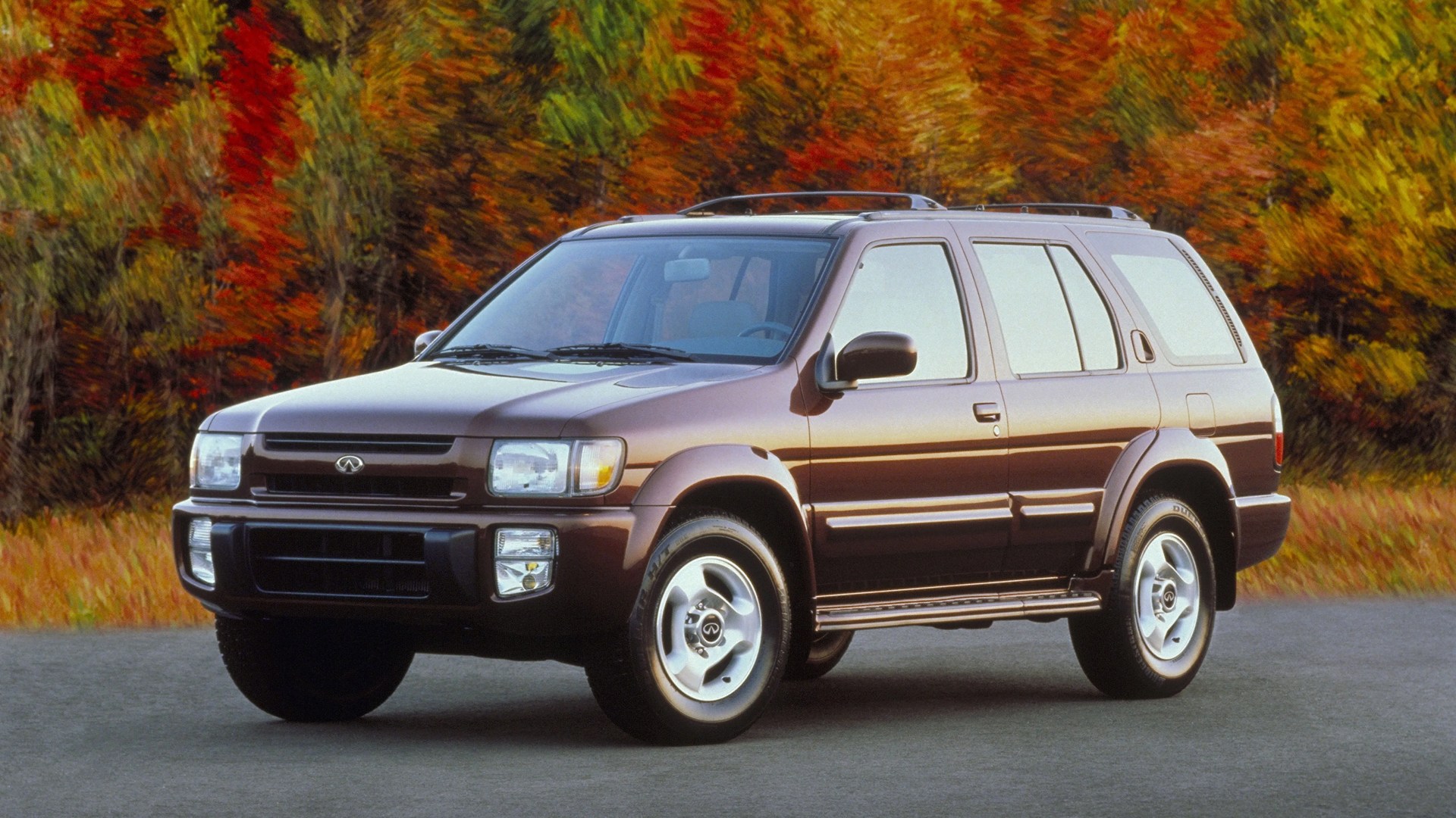 Brown Infiniti SUV parked on a road with autumn foliage in the background.