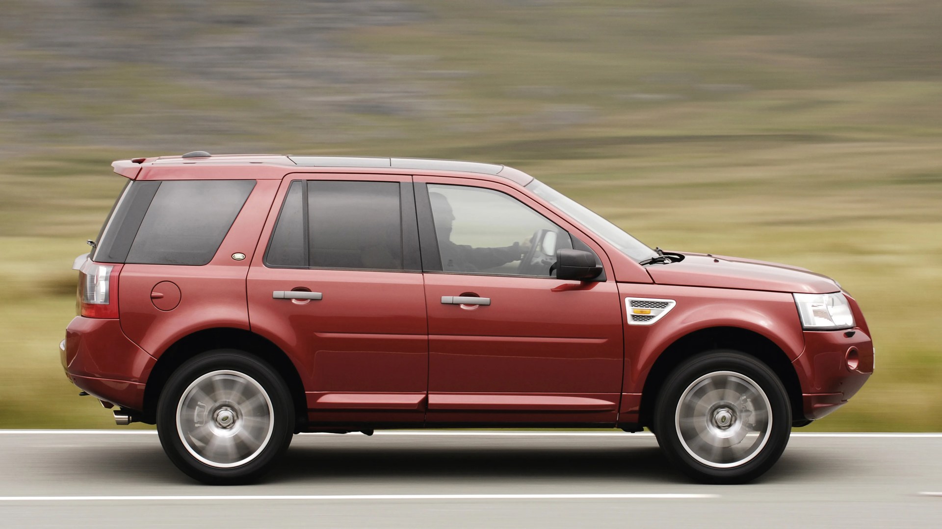 Red mid-size SUV with tinted windows driving on a road with blurred background.