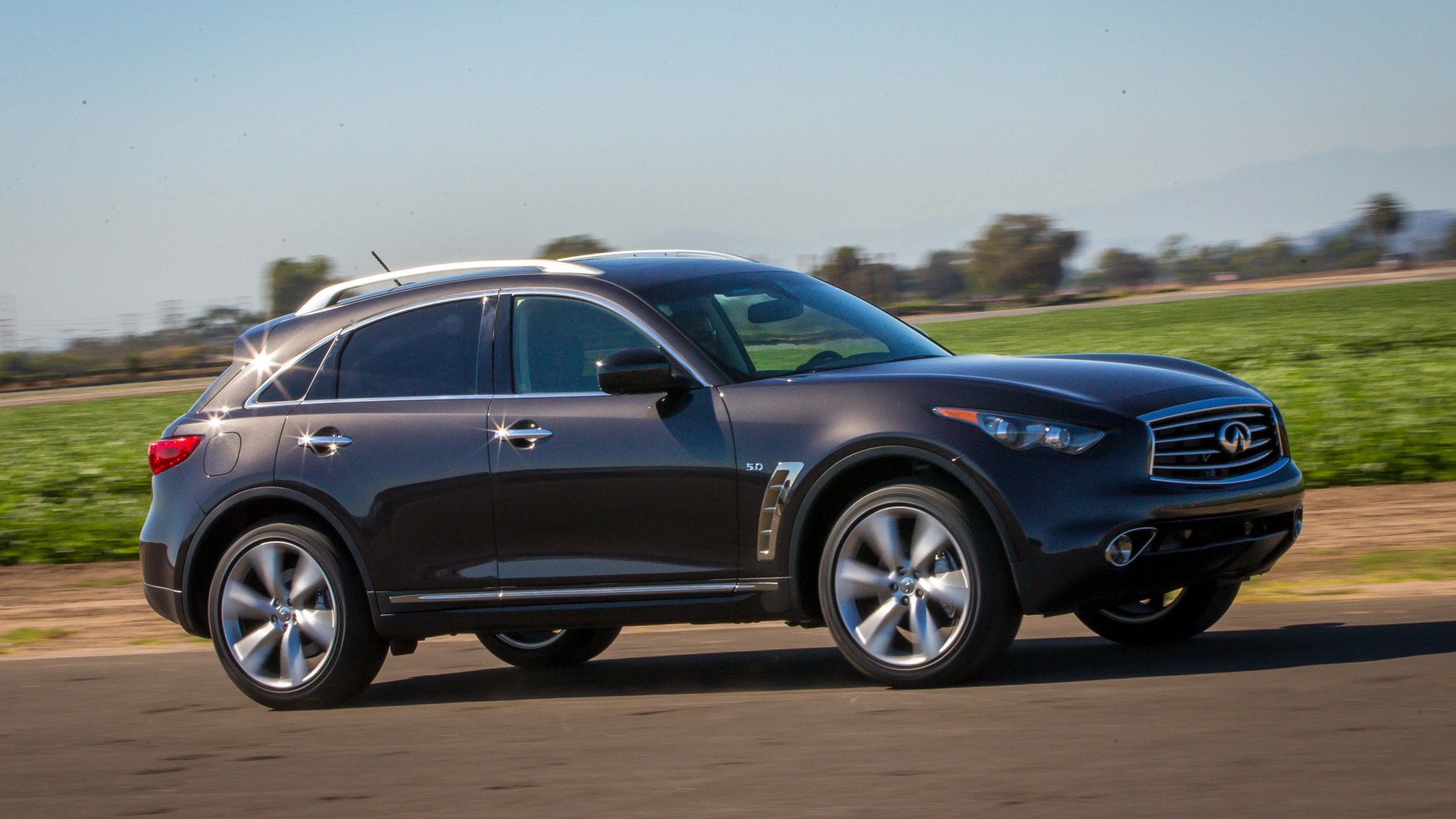 Black Infiniti SUV driving on a paved road with green fields in the background.