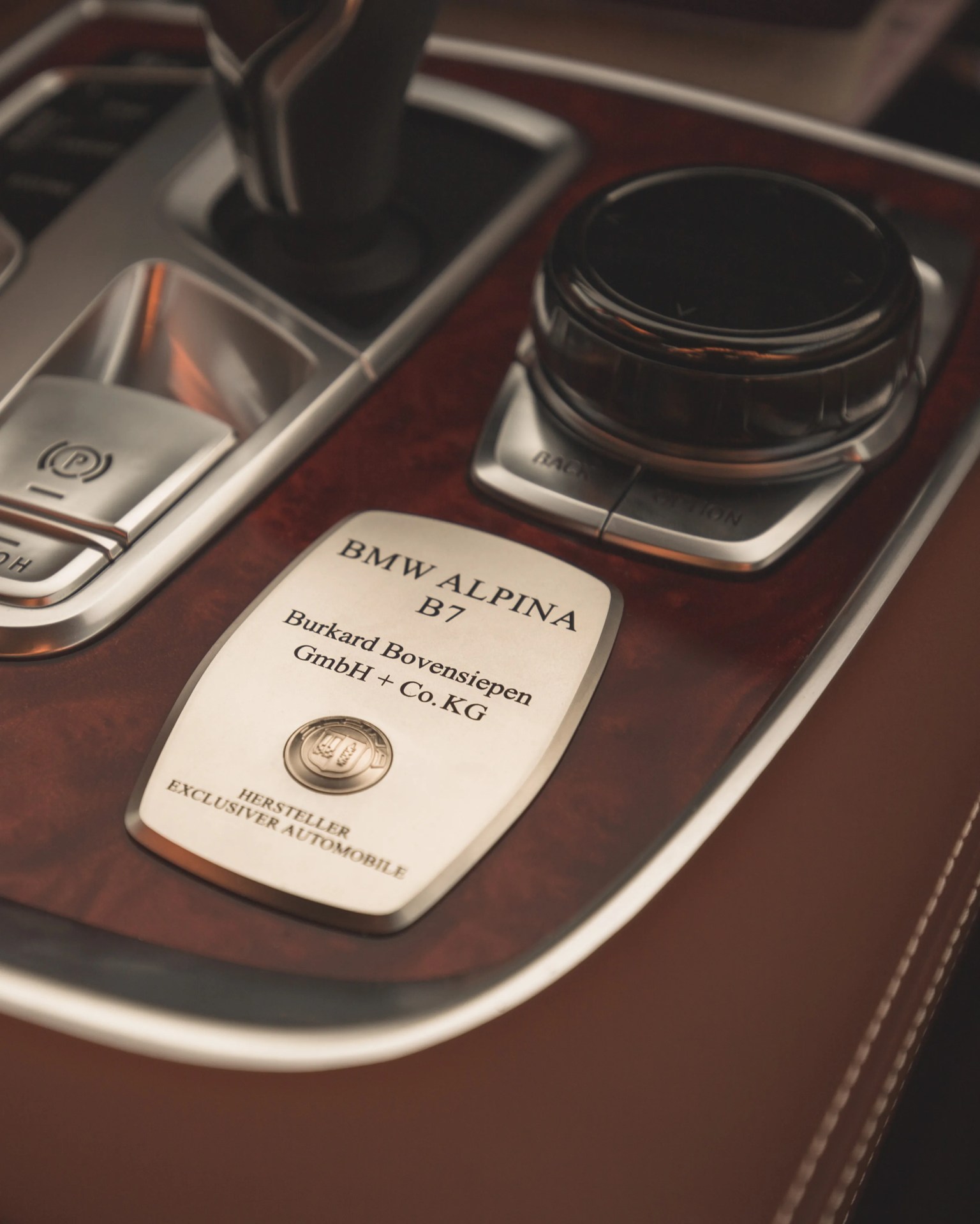 Close-up of a BMW Alpina B7 plaque on a brown wood and leather car center console.