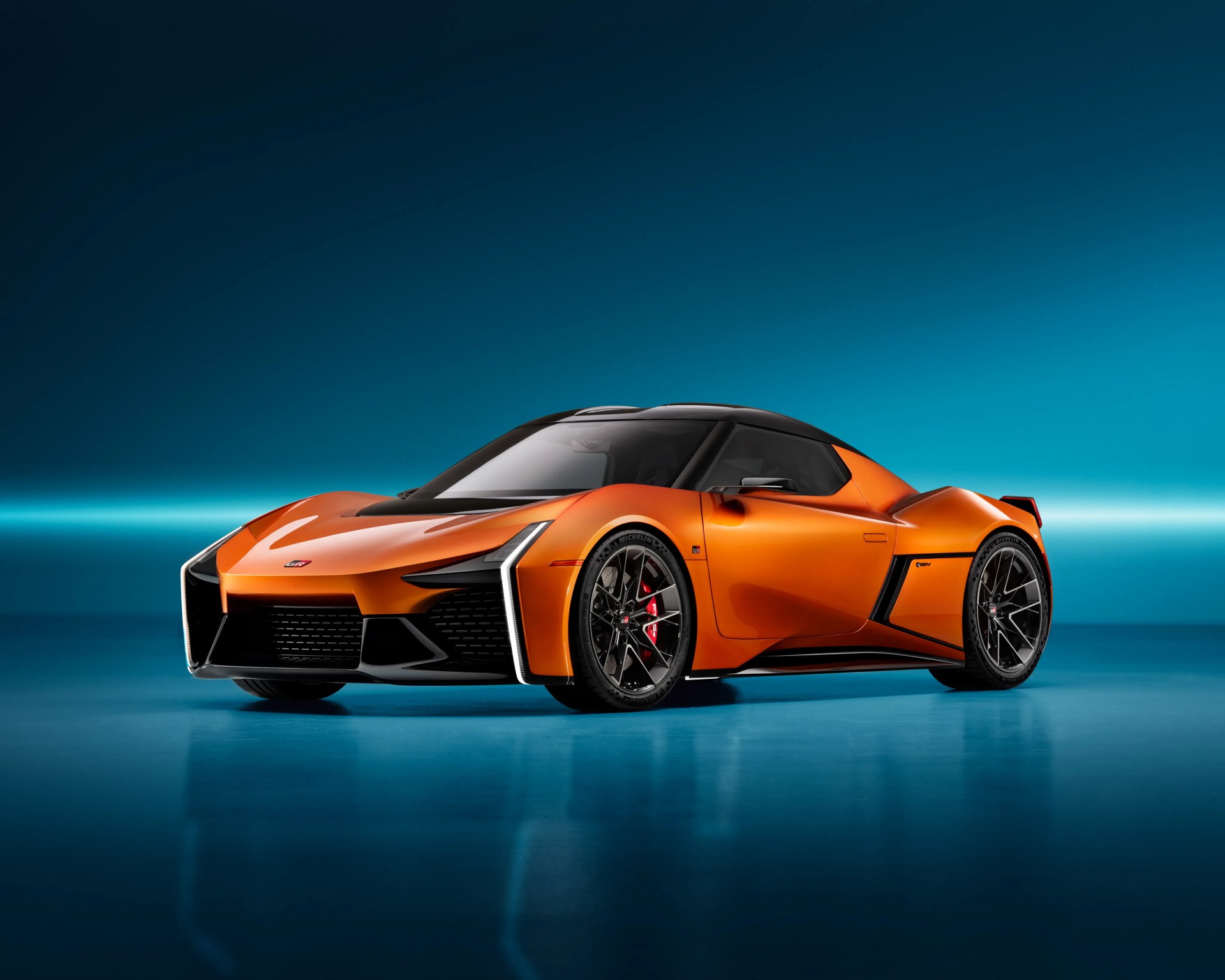 Orange and black futuristic sports car with sharp angular design on a blue reflective floor.