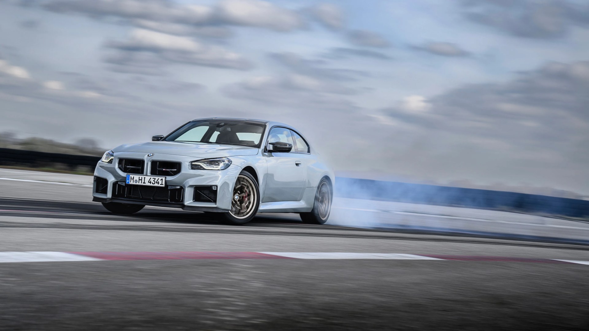 Light blue BMW M2 coupe drifting on a race track with smoke coming from the rear tires.