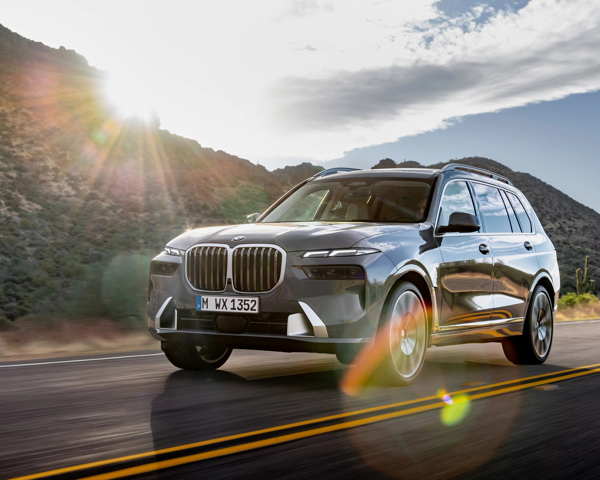 Gray BMW SUV driving on a sunlit road with mountains in the background.