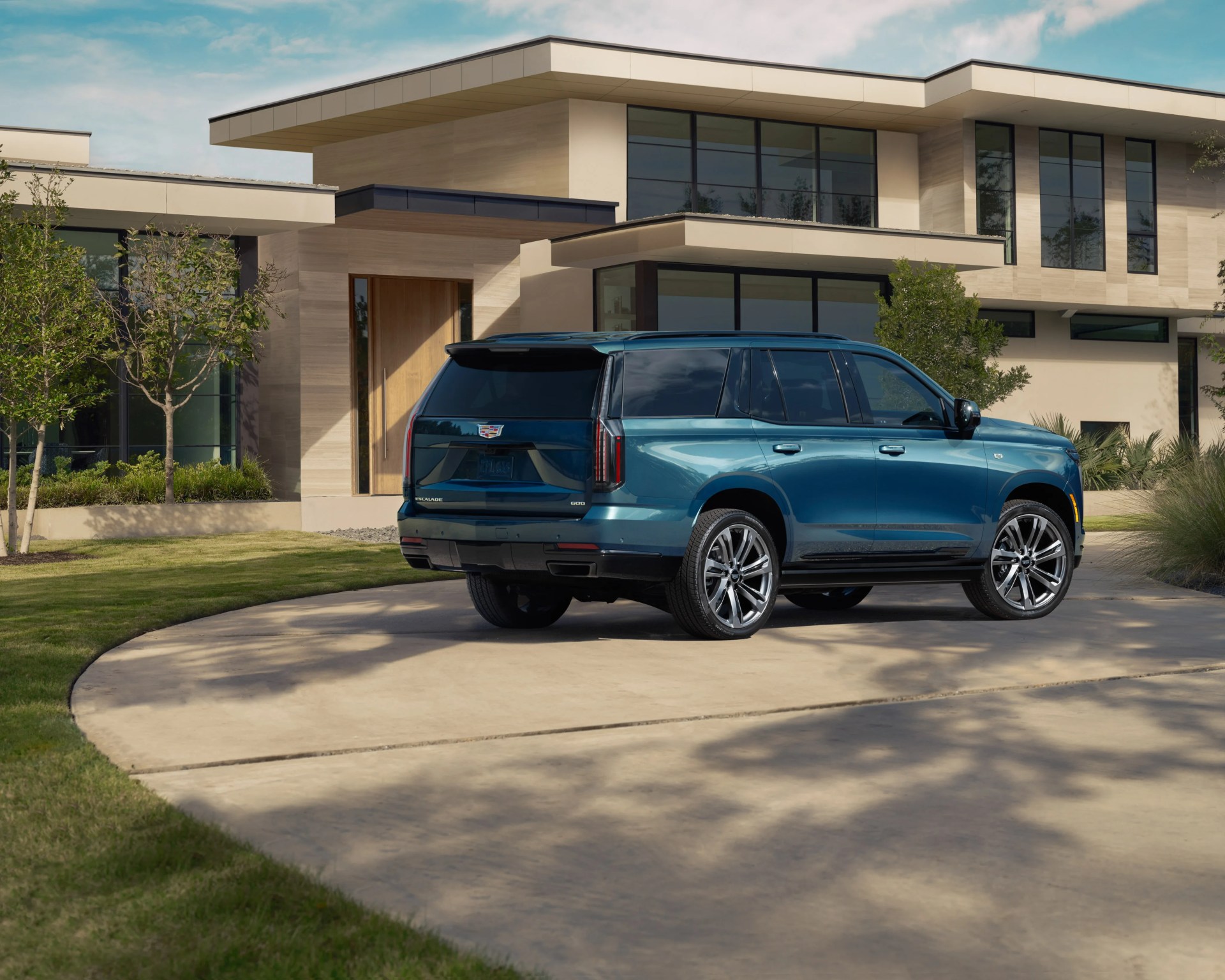Blue Cadillac Escalade SUV parked on a curved driveway in front of a modern beige house.