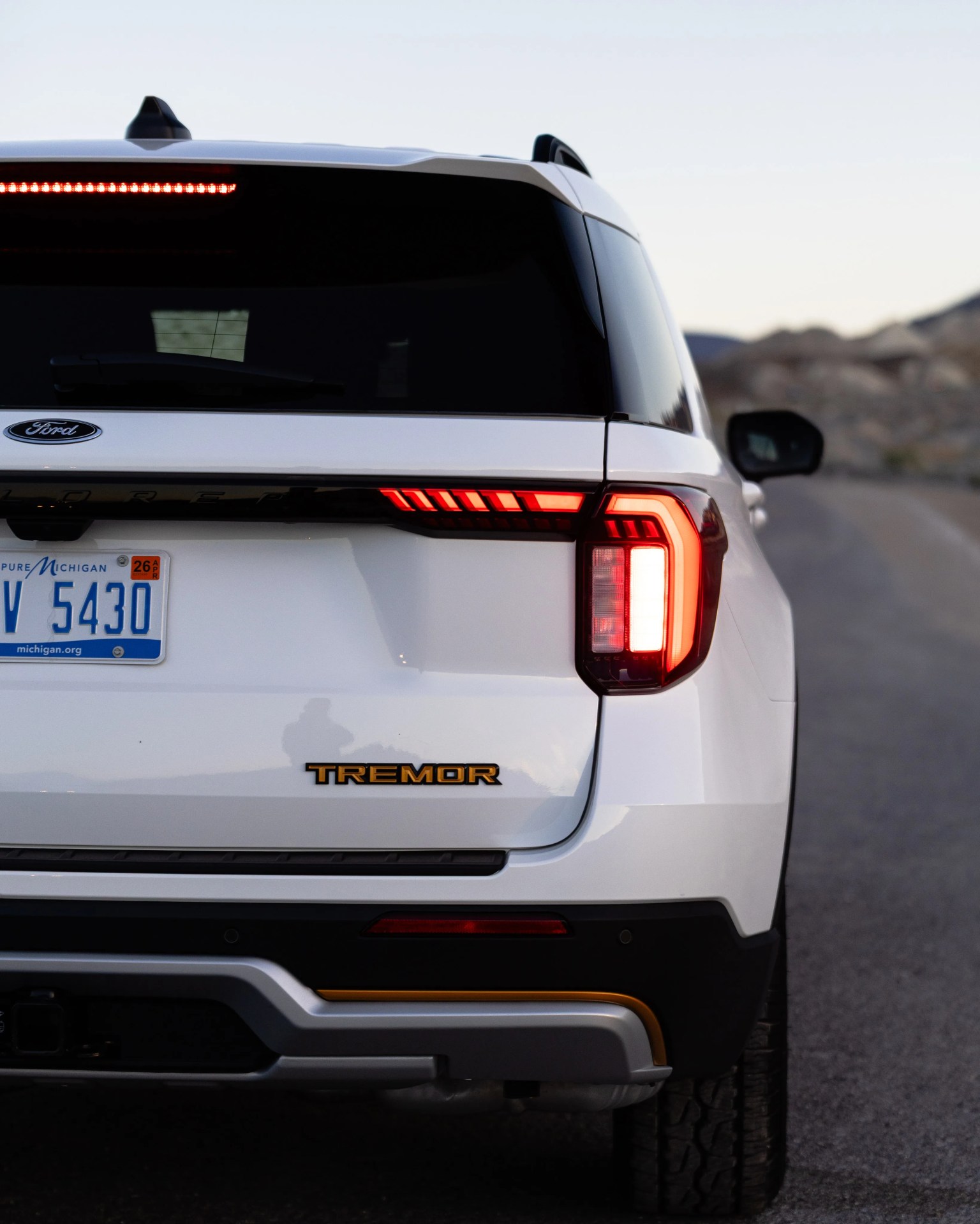 Rear view of a white Ford SUV with Tremor badge and illuminated taillights on a road.