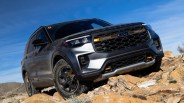 Black and gray Ford SUV with orange accents climbing rocky terrain under a clear blue sky.