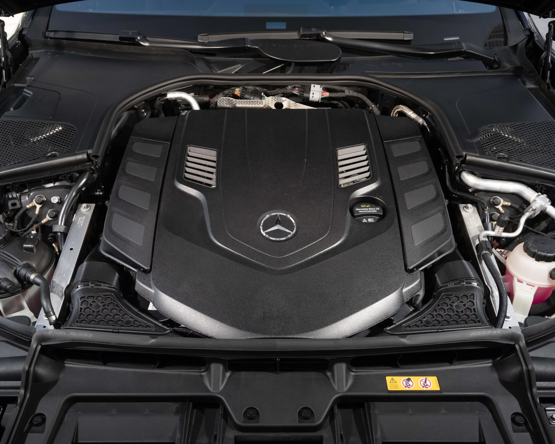Black engine cover with Mercedes-Benz logo and oil cap inside a car engine bay.