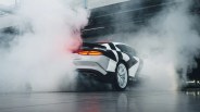 White sports car with black geometric decals performing a burnout, creating thick smoke indoors.