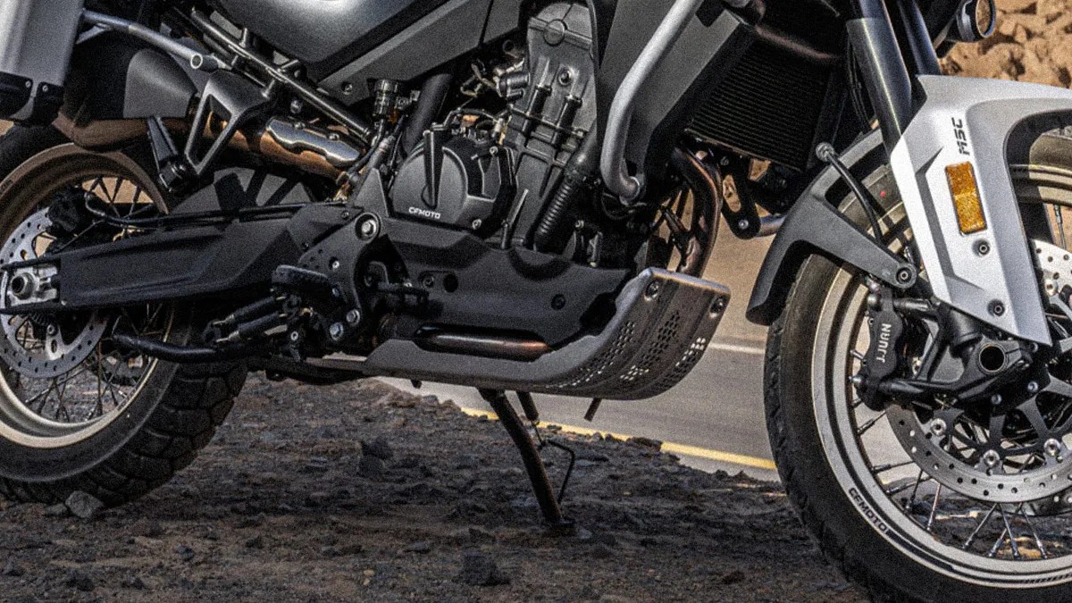 Close-up of a black and silver motorcycle engine and frame with knobby tires on rocky ground.