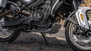 Close-up of a black and silver motorcycle engine and frame with knobby tires on rocky ground.