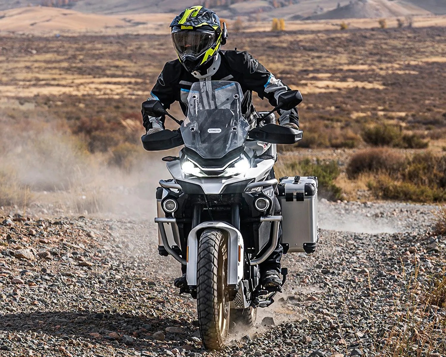 Motorcyclist wearing a black and yellow helmet riding a white adventure motorcycle on a rocky dirt trail.