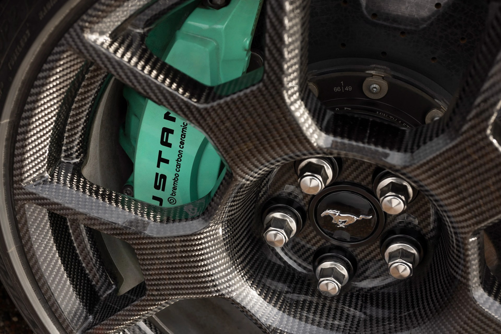 Carbon fiber car wheel with a turquoise Brembo carbon ceramic brake caliper and a Mustang logo center cap.