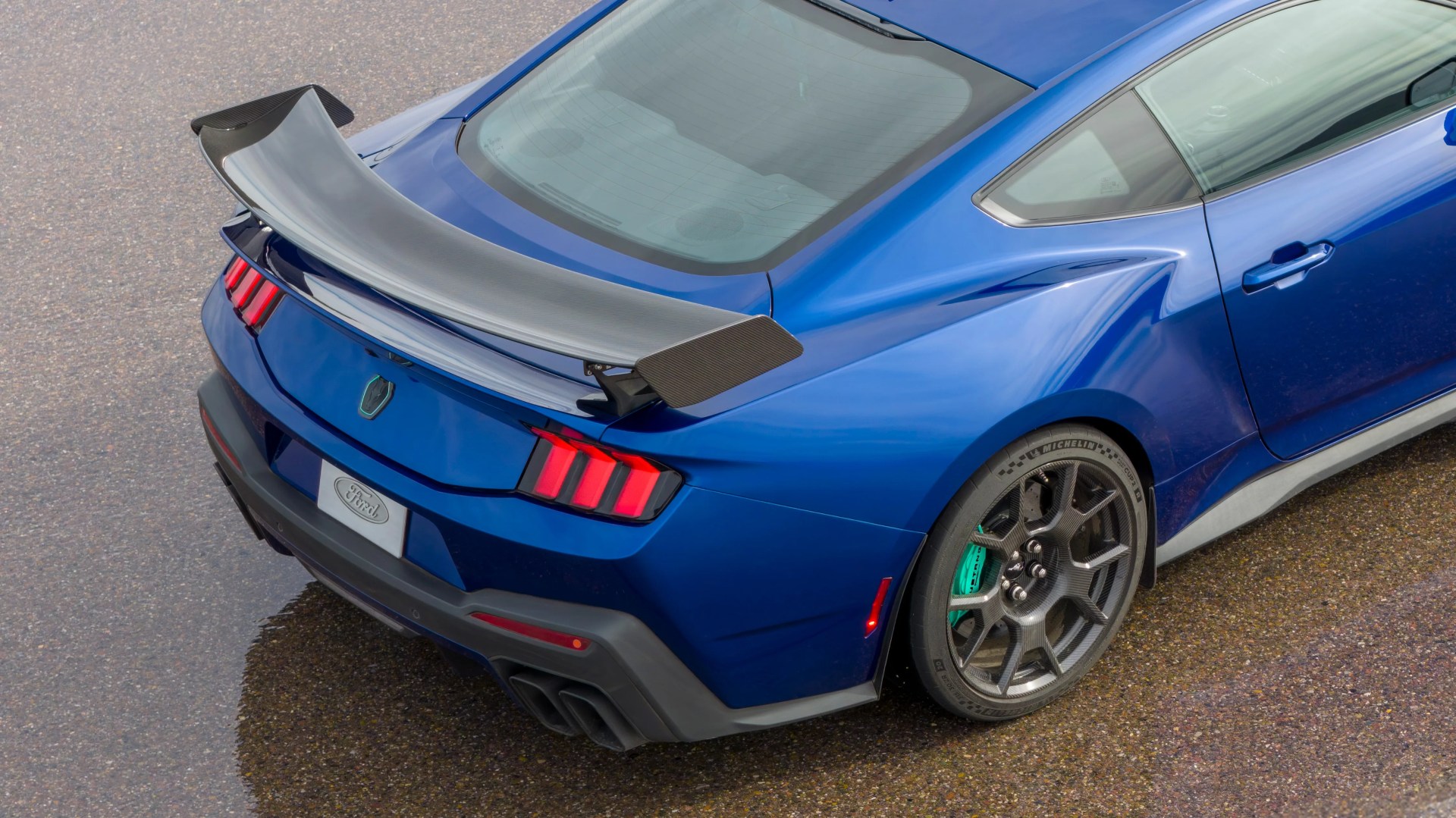 Rear view of a blue Ford sports car with a large carbon fiber rear spoiler and black alloy wheels.