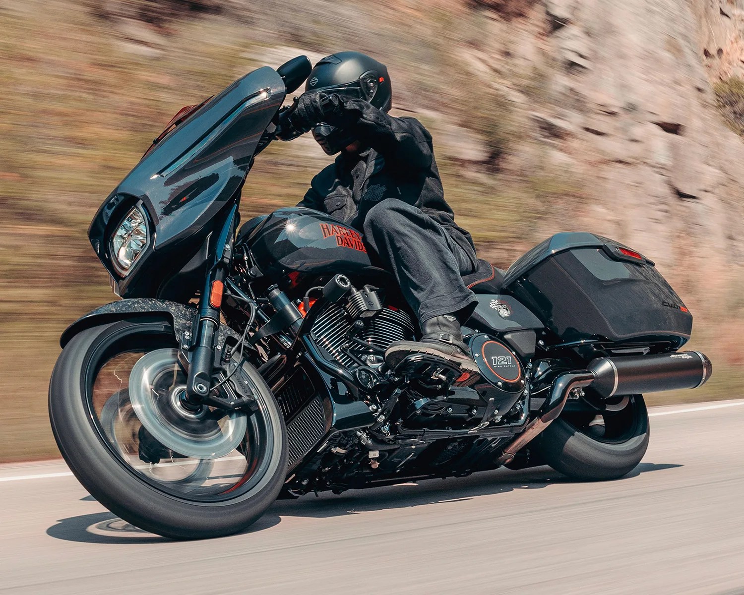 Black Harley-Davidson motorcycle with rider in black gear leaning into a turn on a road.